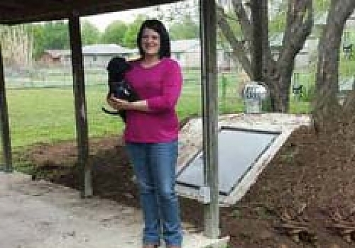 Woman with pet standing in front of a storm shelter